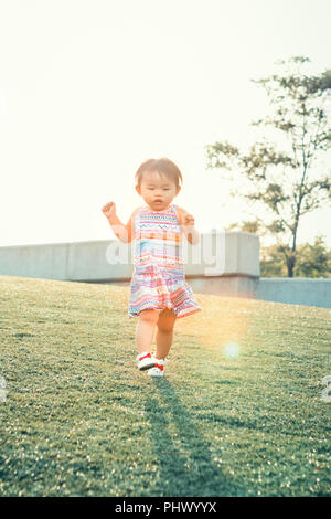 Portrait of a cute adorable little chinese asian vietnamese girl child, one two years old, in dress with ornaments and white shoes, running on field m Stock Photo