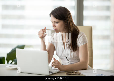 Serious businesswoman drinking coffee while working on laptop in Stock Photo