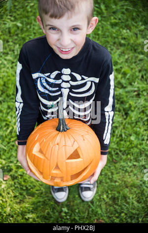 Boy in skeleton costume holding pupmkin at halloween Stock Photo