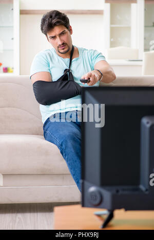 Arm injured man sitting on the sofa watching tv Stock Photo