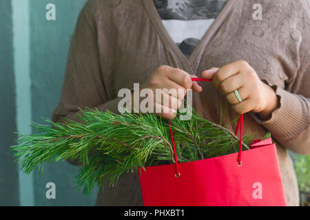 woman in a sweater holding a red package with branches of tree Stock Photo