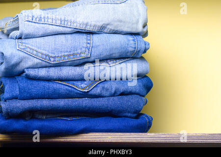 stack  of blue  jeans on a wooden  shelf yellow wall for background Stock Photo