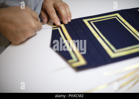 Book binder hand working a pattern on the blue cover of a hardcover book in his workshop in a close up on his hands Stock Photo