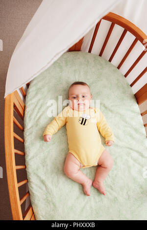 Portrait of cute  funny adorable white Caucasian little baby newborn in yellow onesie lying in crib alone near window, lifestyle candid real life, vie Stock Photo