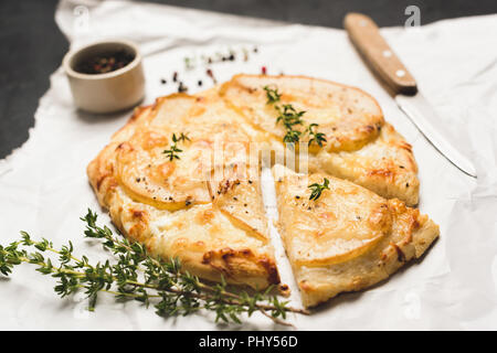 Pizza with pear, cheese and thyme on parchment paper. Mini pizza with pear slice cut out Stock Photo
