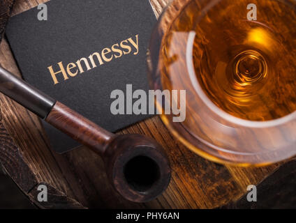 LONDON, UK - SEPTEMBER 04, 2018: Glass of Hennessy Cognac with original coaster and vintage smoking pipe on wooden board. Stock Photo