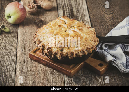 Apple pie in cast iron skillet on rustic wooden table, traditional autumn cozy dessert Stock Photo