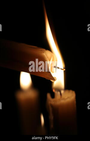 Lighting a candle in the dark, drops of melted wax, flames. Close up. Christmas, New Year greeting card, All Saints Day, All Hallows Eve, church, religion, faith, prayer, holiday, winter fairy tale. Stock Photo