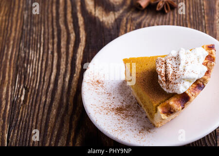 Slices of pumpkin pie with whipped cream on top served on rustic wooden table, close-up, traditional Thanksgiving Day  favorite dessert Stock Photo