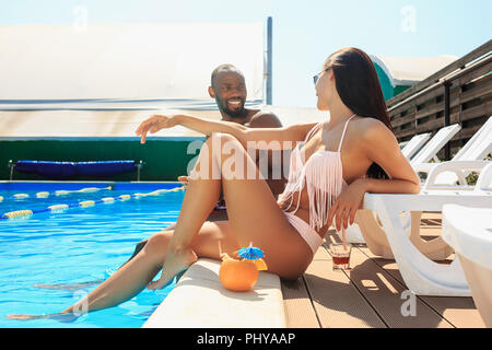 The african man and woman as friends playing and relaxing in a swimming pool during summer holidays. Happy people having fun by the pool. Leisure, swimming, summer, recreation, healthy lifstyle concept Stock Photo