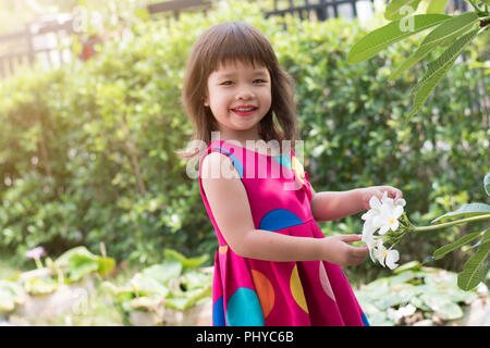 Happy little girl holding plumeria flower on tree. Stock Photo