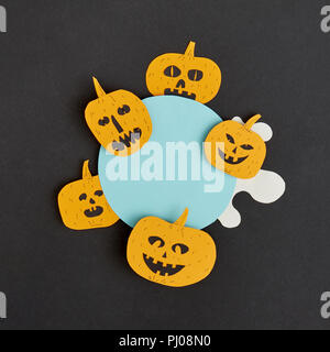 Creative Halloween handmade blue frame with paper horrible smiling and laughing pumpkins on a black paper background. Stock Photo