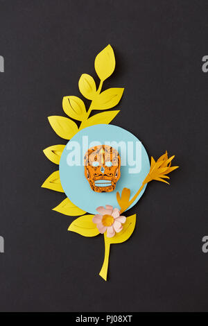 Colorful modern Calaca composition from paper with yellow leaf and decorative skull on a black paper background. Stock Photo