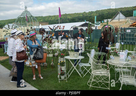 Women standing, looking at display of garden sculpture & furniture on stall at RHS Chatsworth Flower Show, Chatsworth House, Derbyshire, England, UK Stock Photo