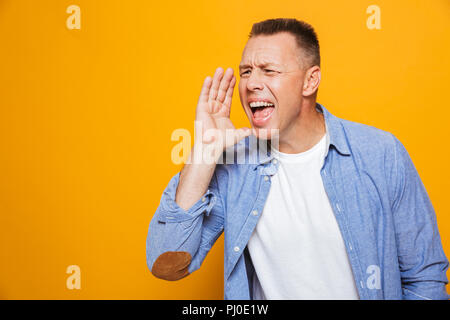 Portrait of a cheerful middle aged man shouting loud isolated over yellow background Stock Photo