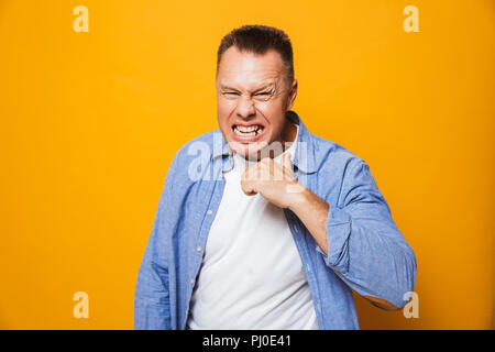 Portrait of an angry middle aged man threatens you isolated over yellow background Stock Photo