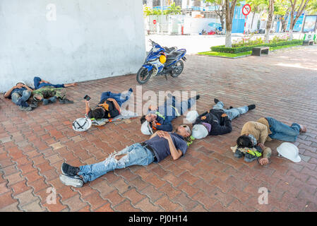 Vietnamese workers relax and sleep lying down on the street, having shoes and construction helmets off, in the shadow of a bridge in Bach Dang Street. Stock Photo