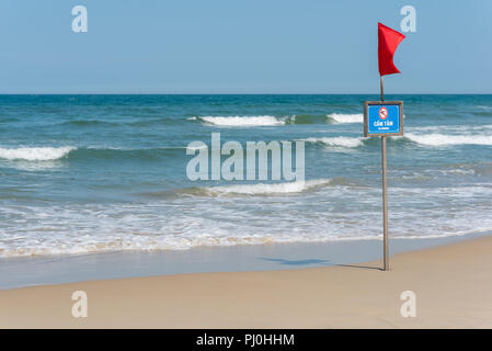 Red flag, the graphic sign and inscription 'No swimming' in English and Vietnamese on My Khe Beach (Da Nang, Vietnam) in May. Stock Photo