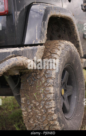 Close up of dirty SUV after driving heavy off-road in wet terrain. Wheels soiled in mud and dirt. Standing on green grass surface. Stock Photo