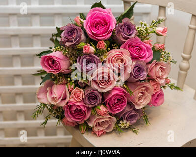 Bouquet of pink roses on an old chair against a white trellis background Stock Photo