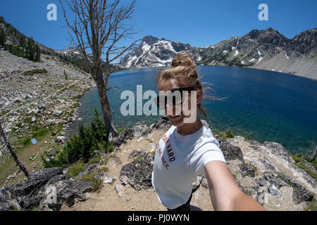 Woman hiker stands on the trail of Sawtooth Lake in Idaho’s Sawtooth Mountain Range in the Salmon-Challis National Forest near Stanley Idaho. Stock Photo