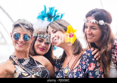 four cheerful beautiful young women celebrate together and take a selfie picture smiling and having fun in friendship. party concept with colored dres Stock Photo