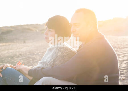nice beautiful middle age 40 years old couple man and woman caucasian hugged and stay together on the beach sitting in the sand and enjoying a golde a Stock Photo