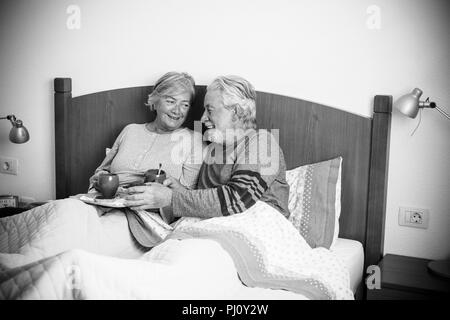 caucasian aged couple doing breakfast at home in the bed. nice natural scene at home for togheterness life concept. love and carefree people married.  Stock Photo