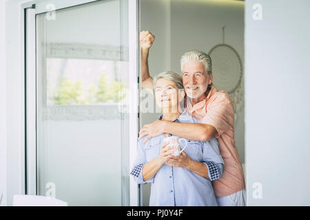 cheerful adult couple at home looking outside together with joy and peace. happy retired caucasian man and woman enjoying his new lifestyle with love  Stock Photo