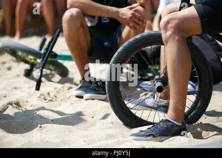 Young BMX rider sitting on bicycle in outdoor park at summer extreme sports festival. Teenager boy rides on specialized bike for performing tricks in  Stock Photo