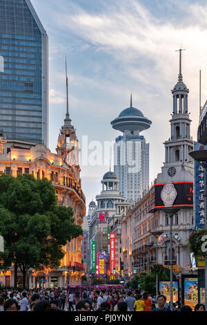 A crowd walks along a street near People's Square in Shanghai China, as the sun sets on a beautiful summer day. Stock Photo