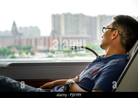 Chinese man sleeps in reclined first class pod on high speed rail from Shanghai to Wuxi. Stock Photo