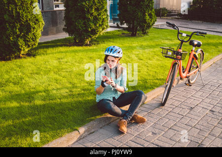 Man and city rolling bicycle, environmentally friendly transport. Beautiful young caucasian woman worker sitting resting on the grass uses a red mobil Stock Photo