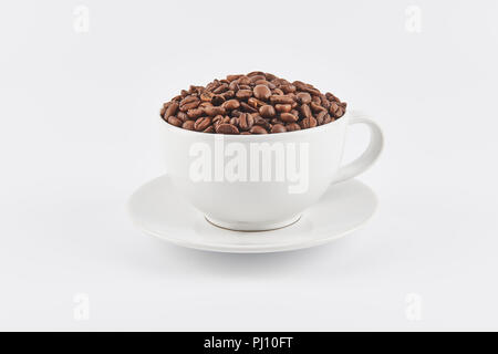 White coffee cup filled with whole coffee beans on a saucer, isolated on white background. Stock Photo