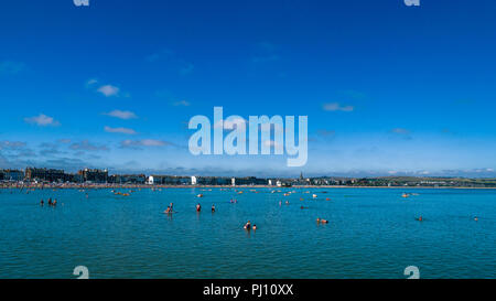 People bathing and taking part in water activities on the shallow waters of  Weymouth Bay, Weymouth, Dorset, England, UK Stock Photo