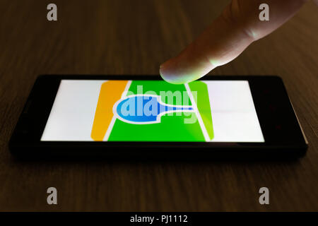 MOSCOW, RUSSIA - August 19, 2018: A smartphone lying on a table in the dark, displaying the logo of the 2GIS app. The finger above touch screen. The c Stock Photo