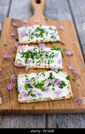 Dairy and lactose-free vegan cream cheese spread made from cashew and macadamia nuts on crackers with fresh chopped chives and edible chive flowers on Stock Photo