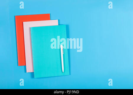 Colorful notebooks and white pen on blue background Stock Photo