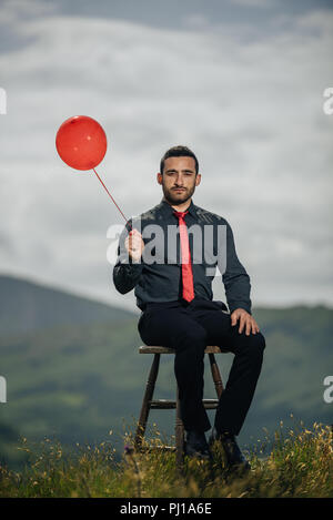 Portrait of a man sitting on a chair holding a balloon, Ireland Stock Photo