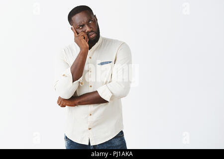 Man recalling recent conversation, feeling doubtful about making right choice. Serious-looking focused and troubled handsome African American in shirt, leaning head on palm and gazing aside, thinking Stock Photo