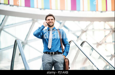 A young businessman going down escalator, talking on the phone. Copy space. Stock Photo