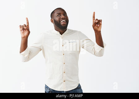 Guy making triumphing dance, signing great deal with business partnerts, lifting hands, pointing up and smiling, in good mood, smiling broadly celebrating successful finish of meeting over grey wall Stock Photo