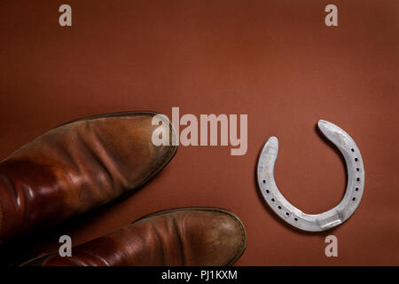 Horseshoe and a pair of leather shoes isolated on a brown background with copy space Stock Photo