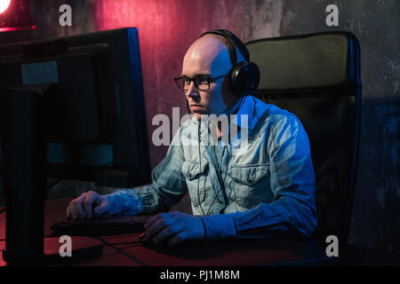 Serious young man sitting and working with computer in dark office Stock Photo