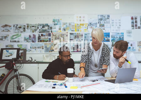 Executives discussing over blueprint at desk Stock Photo