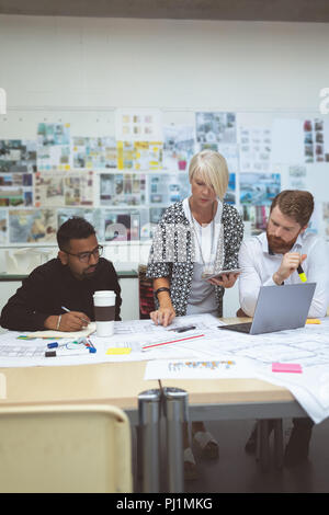 Executives discussing over blueprint at desk Stock Photo