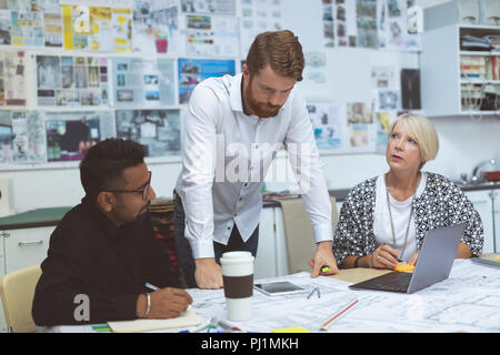 Executives discussing over blueprint at desk Stock Photo
