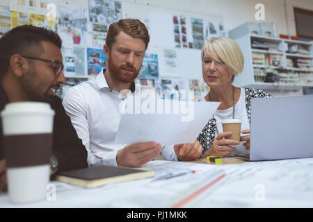 Executives discussing over blueprint at desk Stock Photo