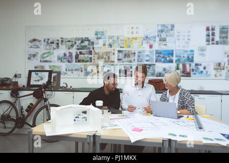 Executives discussing over blueprint at desk Stock Photo