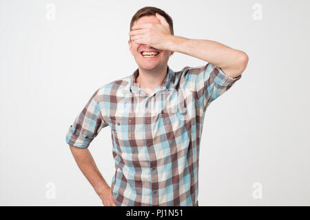 Portrait of a young smiling man covering his eyes with his hand Stock Photo